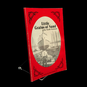 A book titled 'Little Grains of Sand, A History Of The North Peninsula' by Evelyn McCormick with a red cover, author's signature, and a photo of a ship in the background.