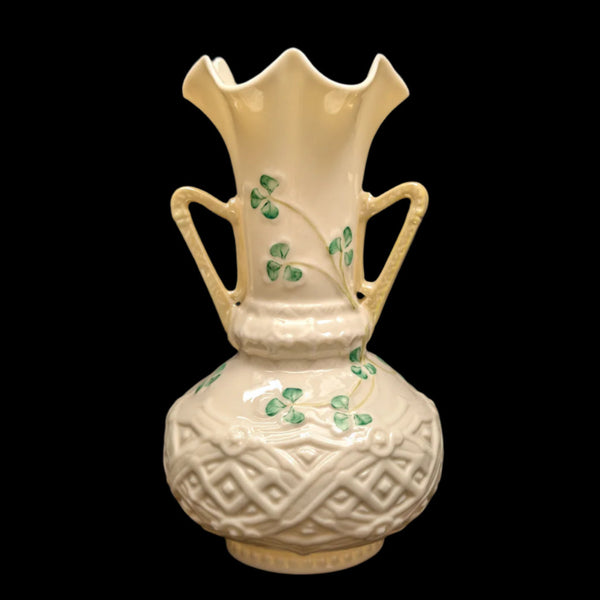 A Belleek porcelain vase with a scalloped rim and handles, featuring shamrock motifs against a cream background.