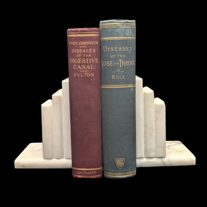 Two vintage medical books from the late 19th and early 20th centuries, placed on a white surface, with bookends on either side.