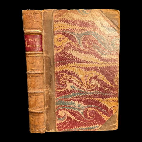 An old book with a decorative cover featuring swirl patterns and the author's name, 'C. Plinius Secundus', printed on the spine.