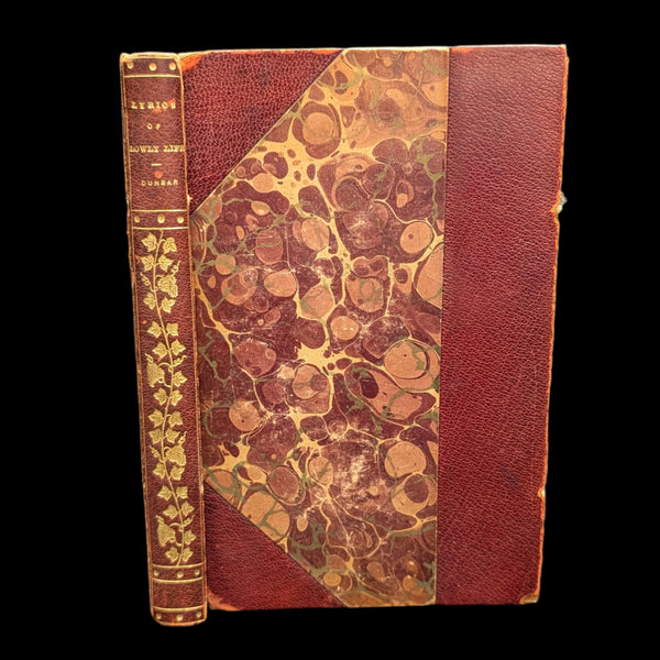 An old book titled 'Lyrics of Lowly Life' by Paul Laurence Dunbar with a decorative floral pattern on the cover. The book appears to be from the early 20th century and has significant tape on the inside binding.