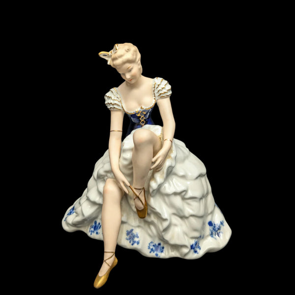A hand-painted porcelain figurine of a woman seated, wearing a blue and white dress with floral patterns and cobalt blue accents.
