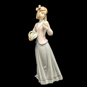 A vintage Lladro porcelain figurine of a woman in a pink dress holding a basket of flowers, with a pink bow in her hair.