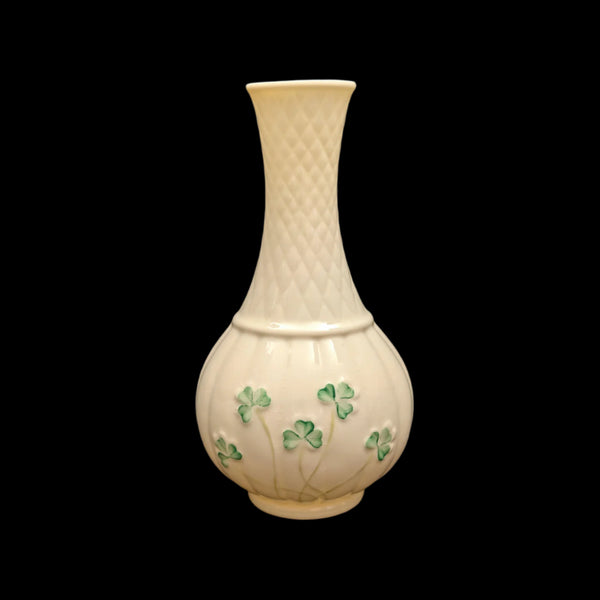 A white porcelain Belleek vase with green shamrock patterns against a black background.
