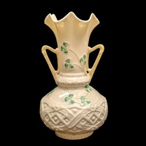 A Belleek porcelain vase with a scalloped rim and handles, featuring shamrock motifs against a cream background.