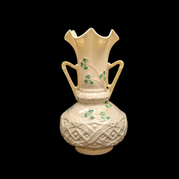 A Belleek porcelain vase with a scalloped rim and handles, featuring shamrock motifs against a cream background.