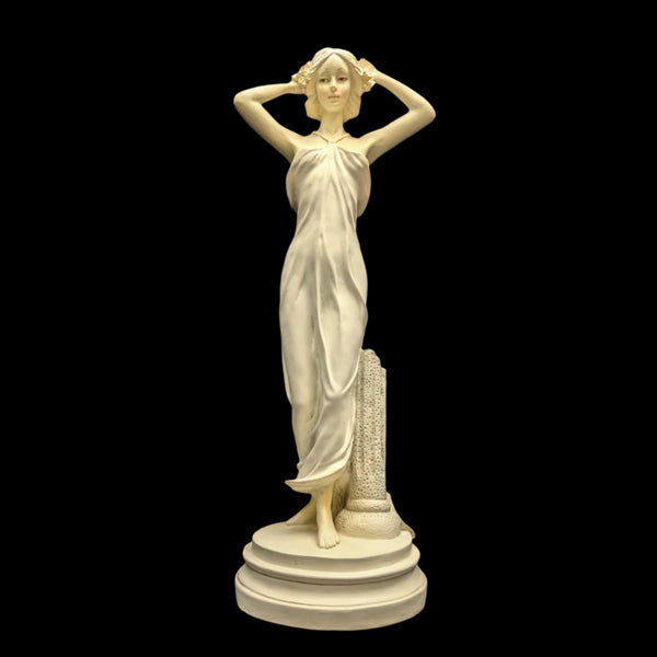 A white resin statue of a woman in a flowing gown, standing on a circular base, with her hands raised to her head.
