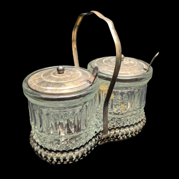 Two crystal sugar canisters with silver plated lids and holders, one larger than the other, featuring intricate designs.