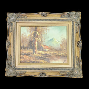 A vintage oil painting depicting a cabin with a red roof nestled in a forest, framed in an ornate wooden frame.