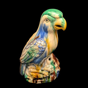 A vintage ceramic figurine of a parrot with Sancai glaze, featuring multiple colors including green, blue, yellow, and brown, perched on a rocky base.