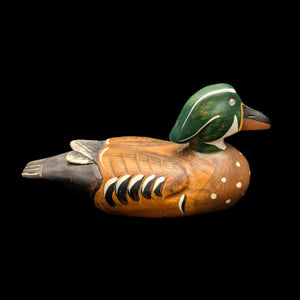 A vintage hand-carved wood duck decoy with a green head, brown body, and multicolored details, displayed against a black background.