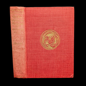 Cover of a hardcover book titled 'The Man That Corrupted Hadleyburg, and Other Stories and Essays' by Mark Twain, with illustrations byung. The cover is red with a gold spiral illustration in the center and a previous owner's inscription in pencil.