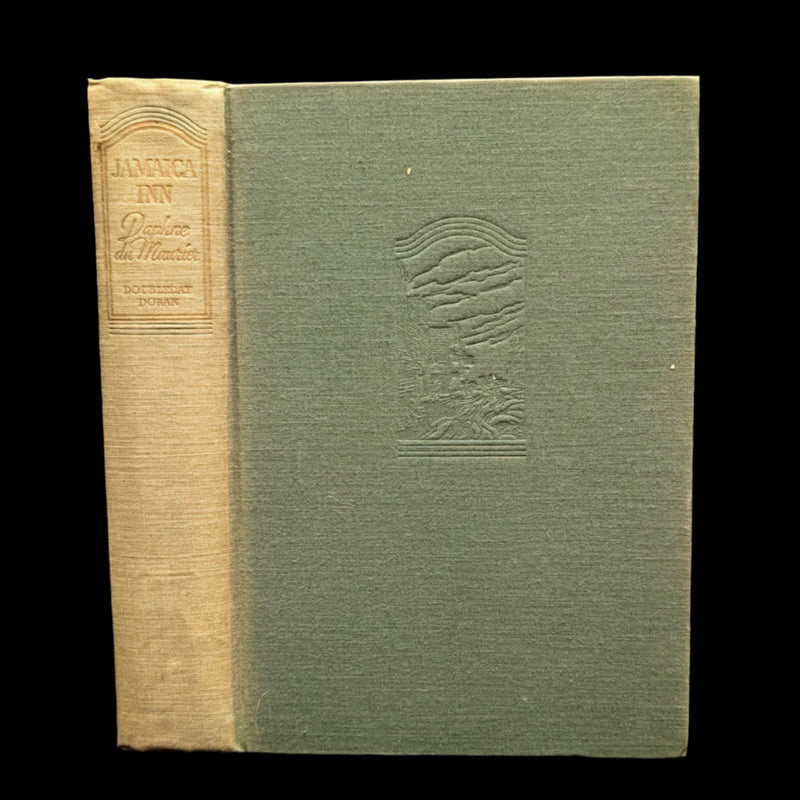 A hardcover edition of 'Jamaica Inn' by Daphne Du Maurier with a visible title and author on the spine, the cover is green with a black and white illustration of a woman's face.
